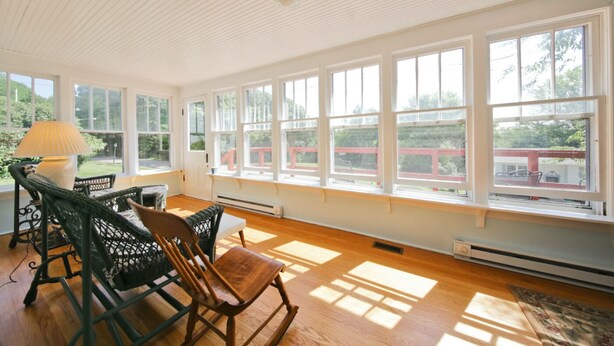 Une pièce lumineuse, baignée de soleil, avec de grandes fenêtres, un plancher en bois et une table entourée de chaises.
