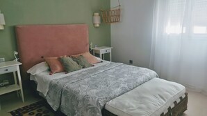 Ein Schlafzimmer mit einem großen Bett, grünen Wänden, einem weißen Nachttisch, einem Rattan-Bettrahmen und einem gemusterten Teppich.