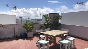 Eine Dachterrasse mit Holztisch und zwei Hocker, umgeben von Blumentöpfen.