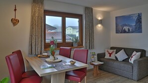 Un coin repas avec une table en bois et des chaises rouges, un canapé gris agrémenté de coussins décoratifs et une fenêtre avec des rideaux.