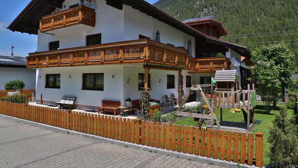 Un chalet à deux étages doté de balcons en bois, d’un espace de jeux et surplombant un paysage montagneux.
