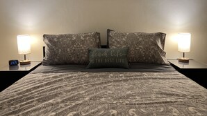 A bed with a patterned bedspread, two matching pillows, a wall-mounted painting, and two bedside lamps. - #1* 5min walk to the Beach, Amazing Virginia Pro Host. (Norfolk)