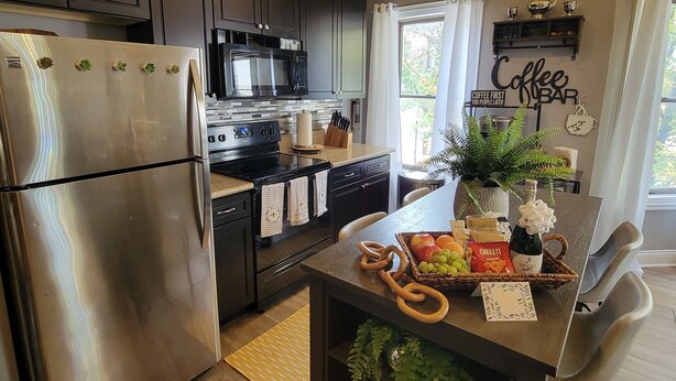 Una cocina moderna con armarios oscuros, electrodomésticos de acero inoxidable y una isla central con una cesta de fruta y una botella de vino.