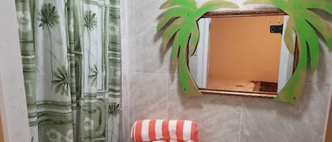 Ett badrum med en toalett, ett handfat, en spegel med en grön ram som föreställer ett palmträd och en duschdraperi med ett blommönster.