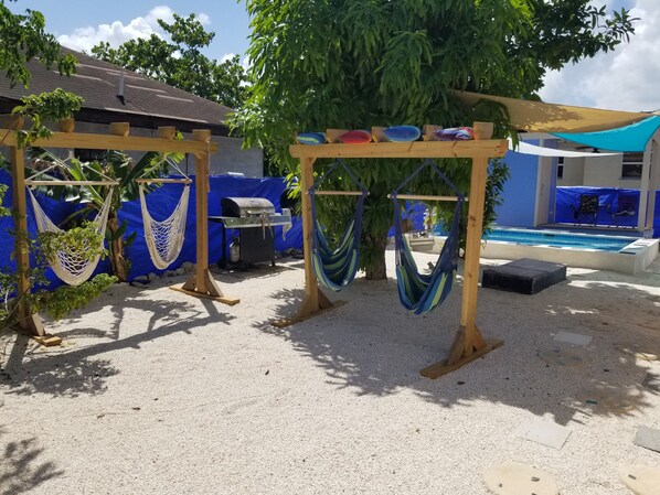 A backyard with hammocks, a barbecue grill, and a pool.