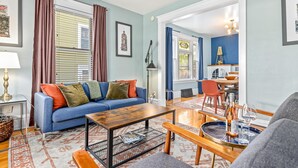 Uma sala de estar com um sofá azul, uma mesa de centro de madeira e um espaço de jantar com mesa e cadeiras.