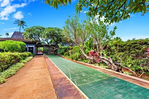 A green shuffleboard court with a pathway leading to a building with a sloped roof.