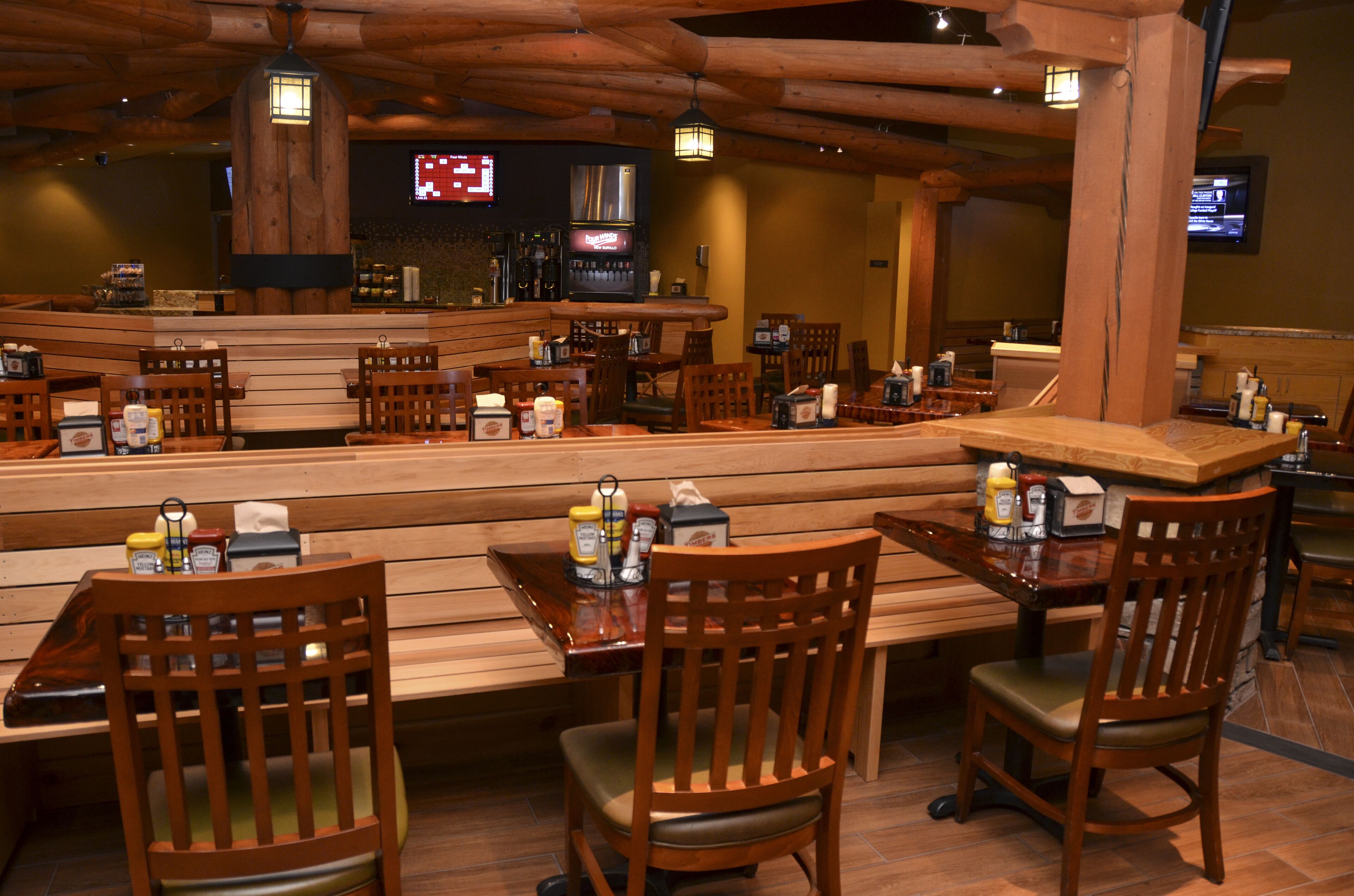 Un restaurante con mobiliario de madera, una zona de bar y una pantalla digital mostrando contenido.