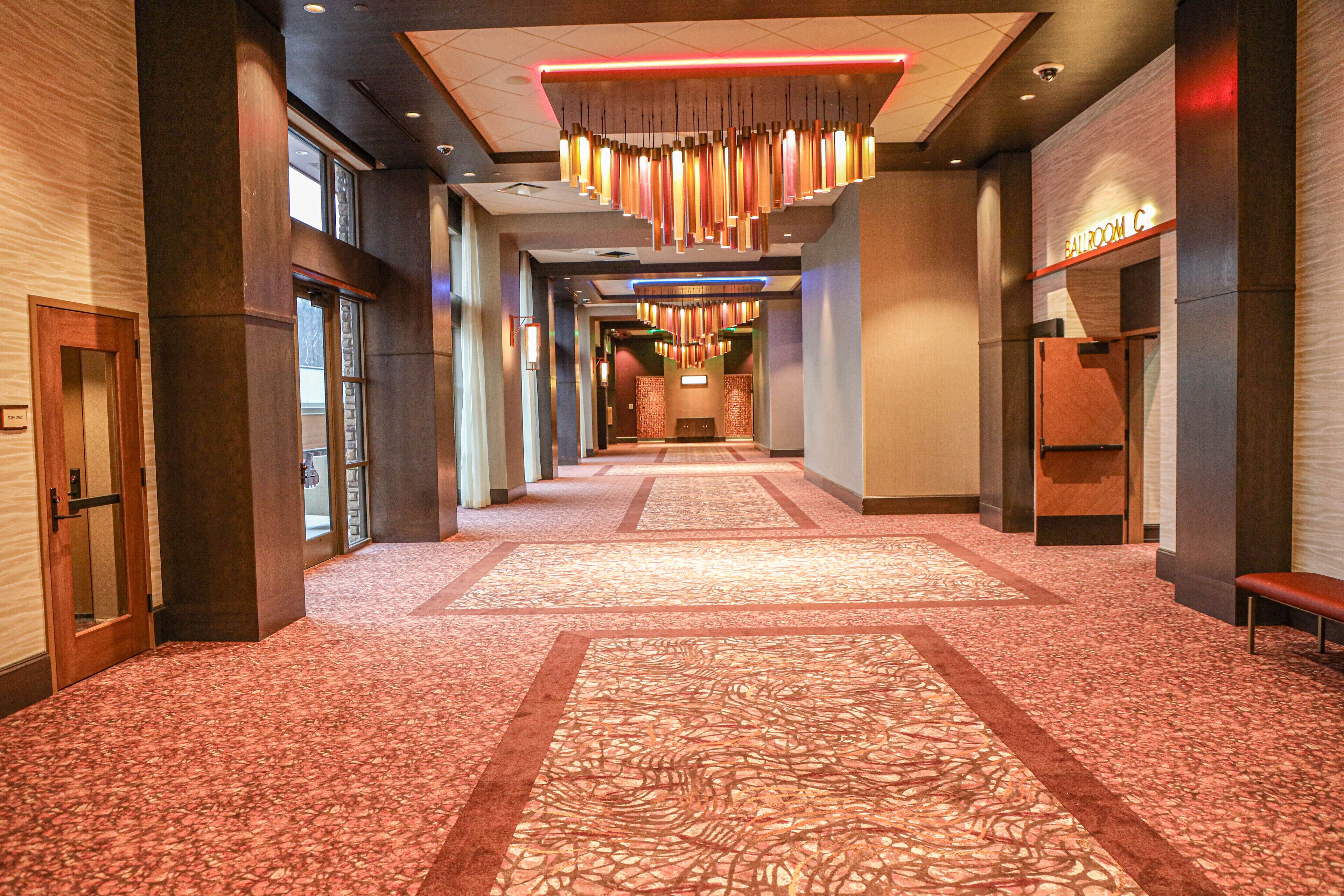 A hotel corridor with patterned carpet, modern chandeliers, and a visible bathroom on the right.
