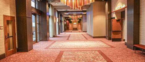 A hotel corridor with patterned carpet, modern chandeliers, and a visible bathroom on the right.