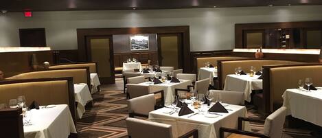A restaurant with multiple tables and booths, each with white tablecloths and set with wine glasses and cutlery.