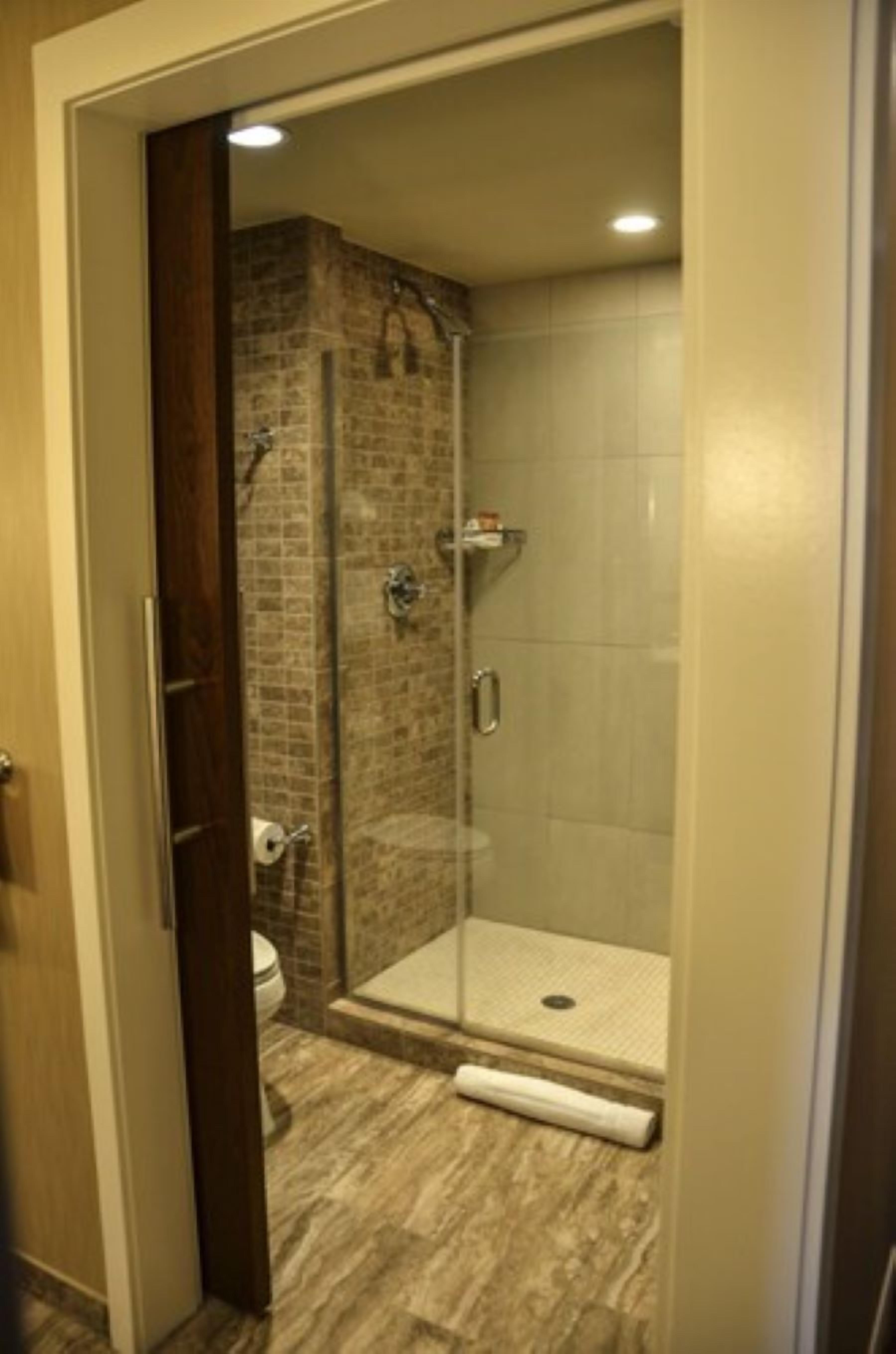 Una zona de ducha con puerta de vidrio, pared de ladrillo y suelo de baldosas.