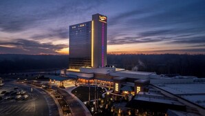 Um hotel grande com uma placa vertical chamativa, vários estacionamentos e uma área de entrada bem iluminada.