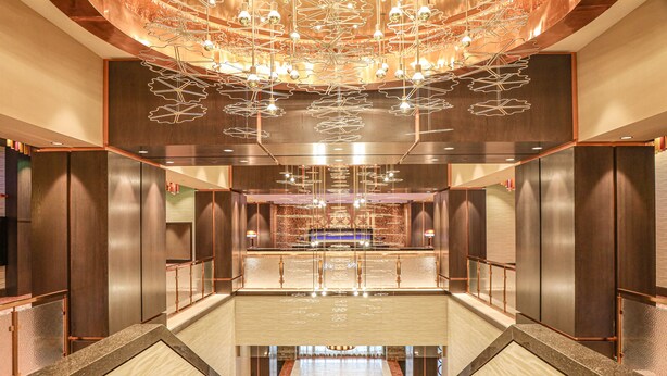 Um hall de hotel moderno com uma recepção central, um lustre grande e um chão refletor.