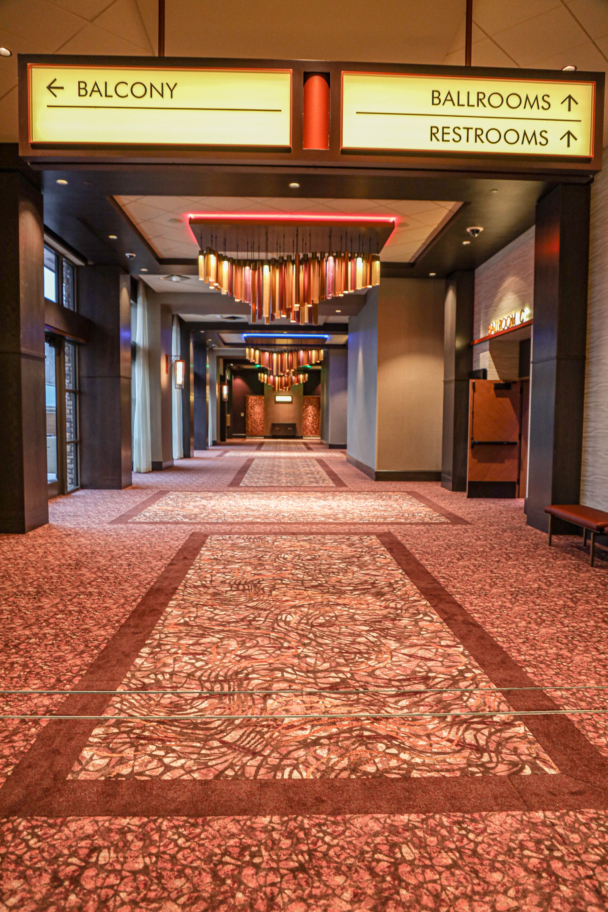 A hotel corridor with directional signs to the balcony, ballrooms, and restrooms.