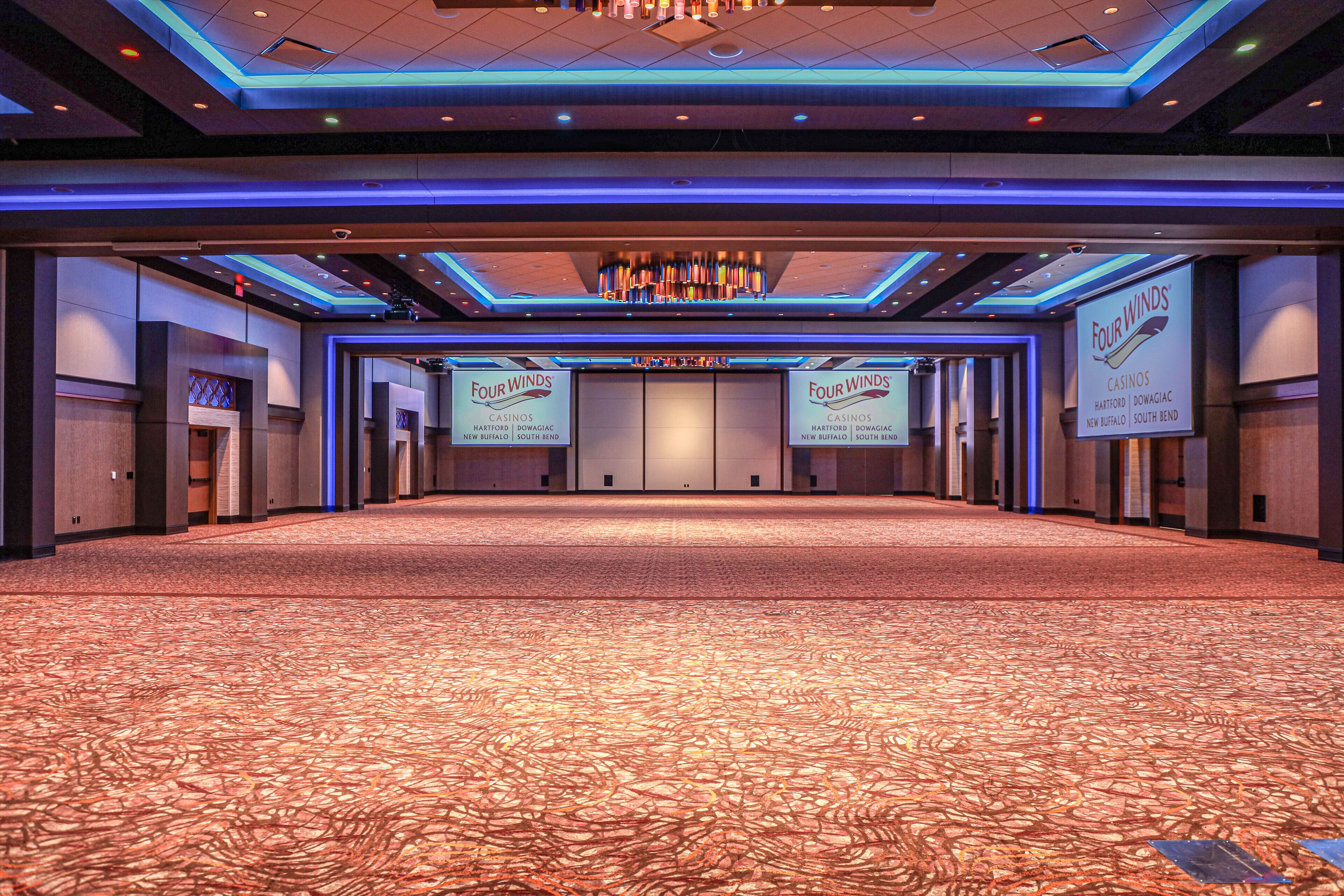 A spacious conference room with a patterned carpet, blue ambient lighting, and banners for Four Winds Casinos.