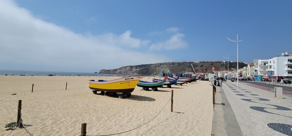Une plage où plusieurs bateaux aux couleurs vives sont amarrés sur le sable, avec un ciel dégagé et une chaîne de collines en arrière-plan.