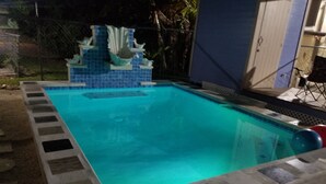 Une piscine dont le bord est revêtu de carreaux bleus et qui est agrémentée d’une cascade décorative.