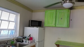 Une cuisine équipée d’un four à micro-ondes, d’un réfrigérateur, d’un évier, de meubles de rangement en bois, d’une fenêtre avec des stores et d’un ventilateur de plafond.