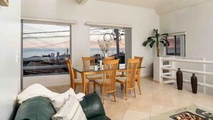 A modern living room with a green sofa, a dining table with chairs, and large windows offering a city view. - Beautiful home in playas de Tijuana (playas de tijuana)