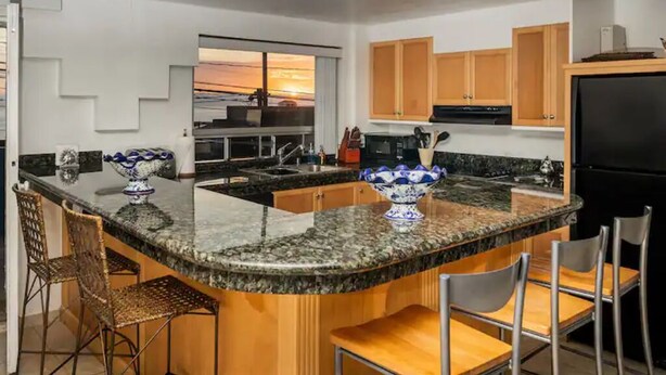 A modern kitchen with granite countertops, wooden cabinets, and a large island with bar stools. - Beautiful home in playas de Tijuana (playas de tijuana)