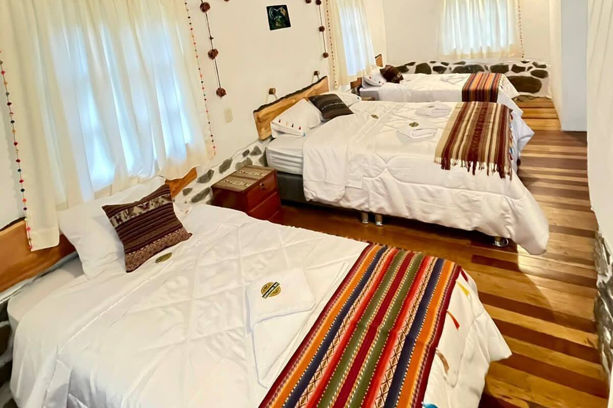 Una habitación acogedora con vigas de madera, tres camas con ropa de cama blanca y suelo de madera.