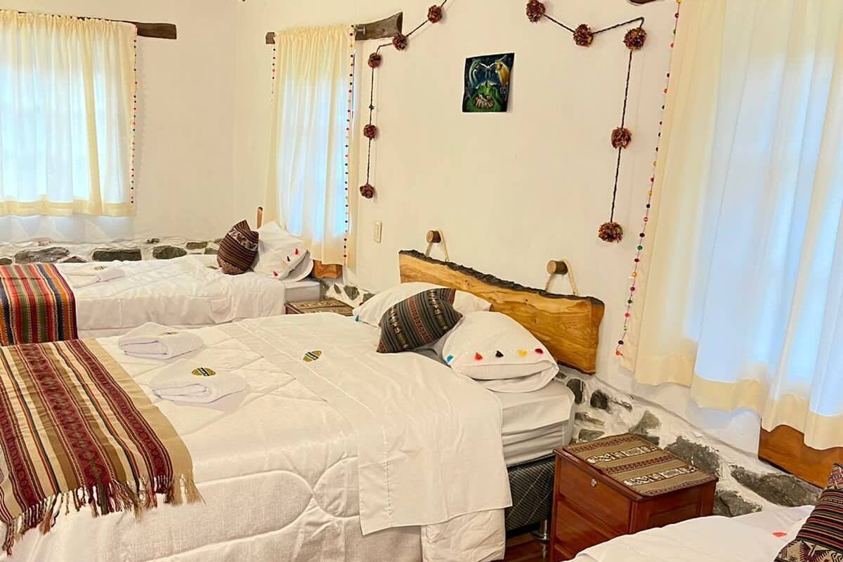 Habitación de hotel con tres camas, vigas de madera en el techo y pared de piedra.