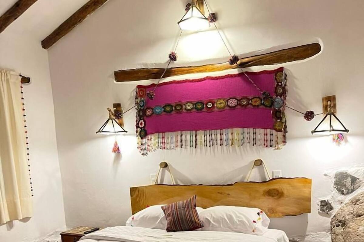 Un dormitorio acogedor con cabecera de madera, manta a rayas coloridas y un tapiz decorativo sobre la cama.