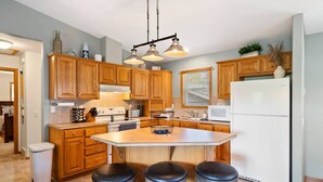 A kitchen with wooden cabinets, a white refrigerator, a large island with stools, and pendant lighting. - Cozy Lake Alice Cottage Next to Trails & WI River! Pet Friendly! (Tomahawk)