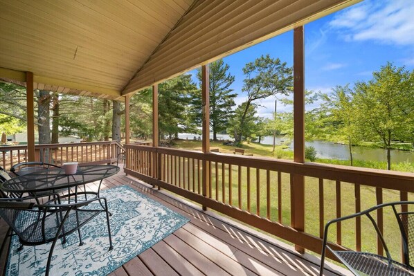 A covered outdoor area with a table and chairs, a view of a lake, and a wooden deck.