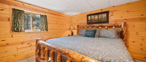 A wooden cabin bedroom with a bed, curtains, a painting, and a fireplace.