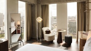 A hotel room with a large bed, a sitting area with a chair and ottoman, a small round table, and a large mirror.