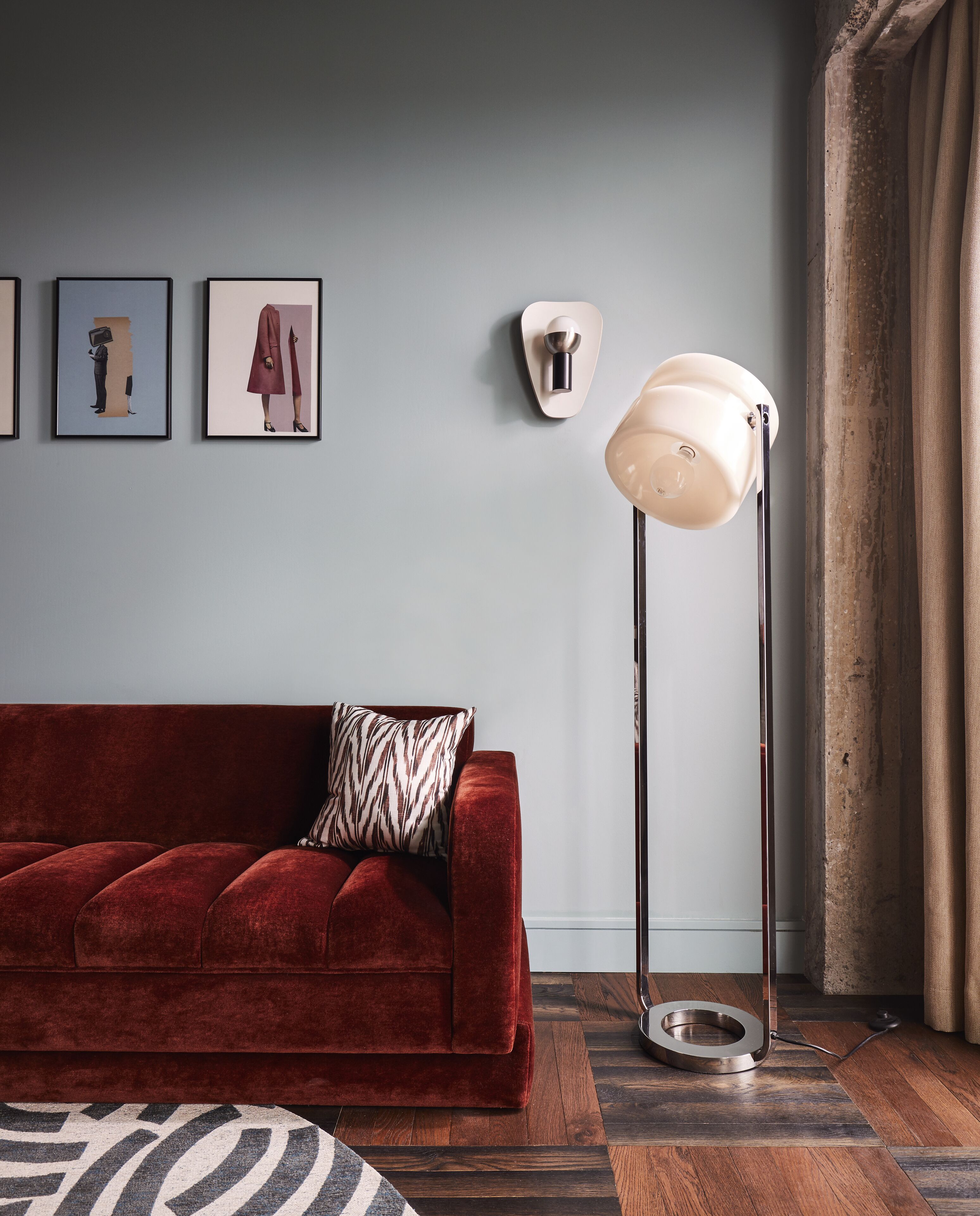 A red velvet sofa with a zebra-patterned pillow, a floor lamp, and three framed artworks on the wall.