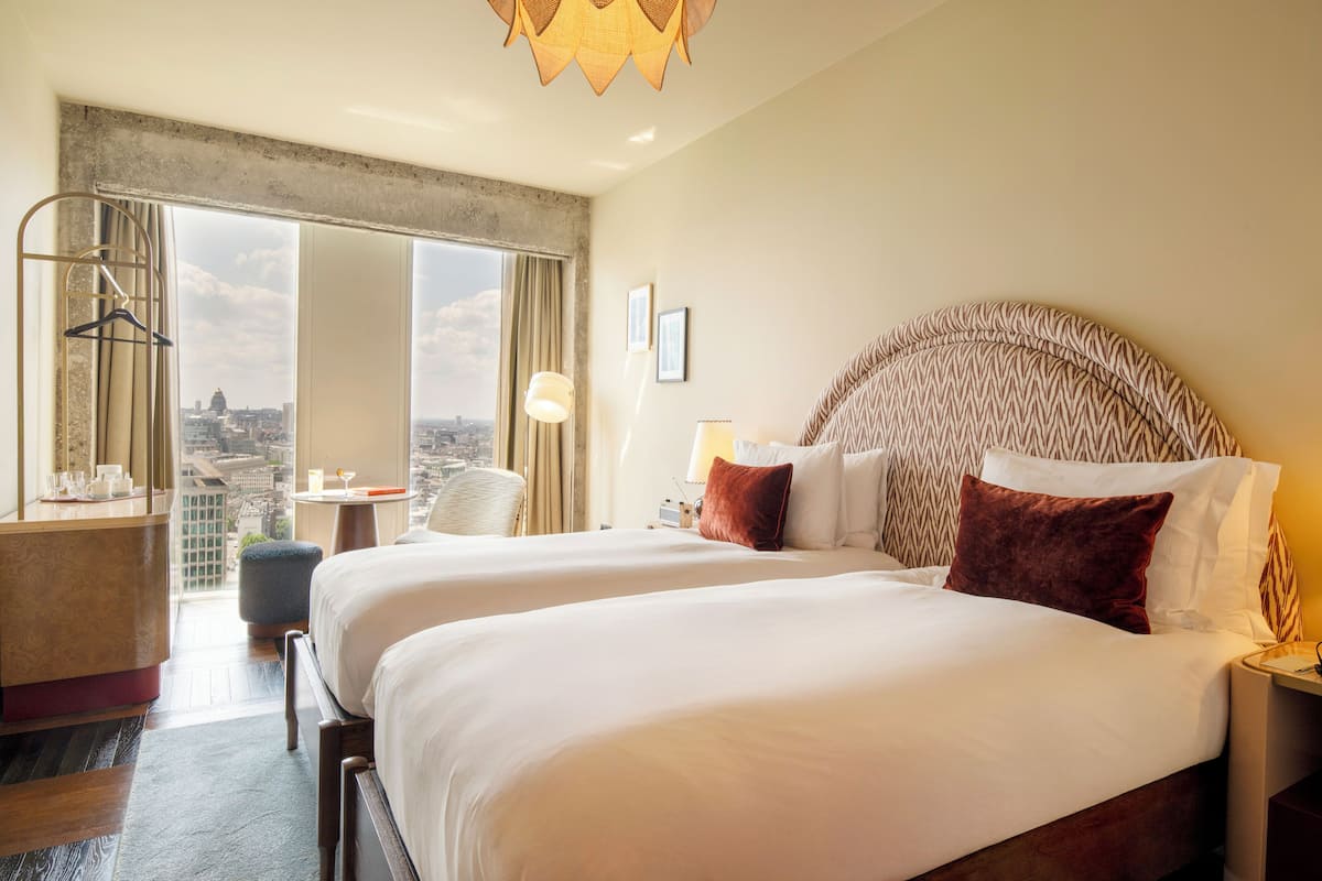 Quarto de hotel com duas camas, vista para a cidade, uma cadeira suspensa e um minibar.