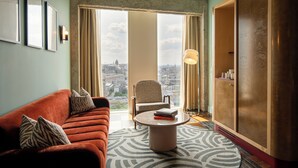 A hotel room with a large window, a sofa, a chair, a round coffee table, and a wardrobe.