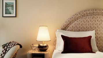 Una cama bien hecha con un almohadón rojo, una lámpara de noche y un cuadro en la pared.