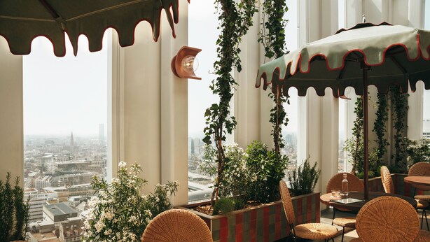 A rooftop terrace with wicker chairs, a table, and a view of the cityscape.
