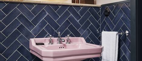 A bathroom with a pink sink, a mirror with a gold frame, and a dark blue herringbone-patterned wall.