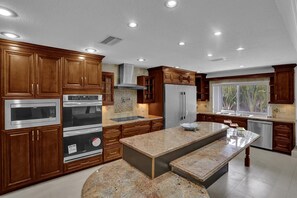 Une cuisine moderne dotée de meubles en bois, d’appareils électroménagers en acier inoxydable, d’un plan de travail en granit et d’une fenêtre donnant sur un paysage verdoyant.