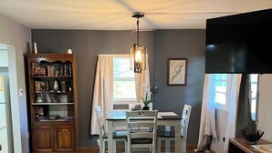 Un coin repas avec une table et des chaises, un meuble en bois contenant des livres, un ventilateur de plafond et un téléviseur.