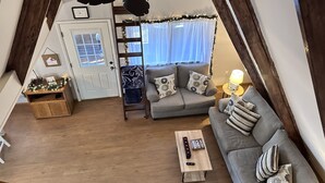 Un salon de style industriel, avec un plancher en bois, un canapé gris, une table basse en bois, un ventilateur de plafond et un escalier menant à un niveau supérieur.