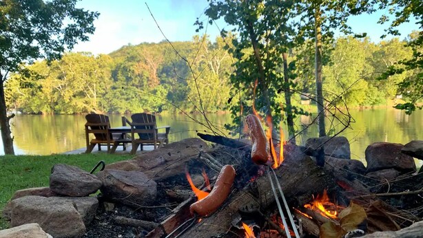 Un feu de camp avec des saucisses en train de cuire, entouré de rochers et de bûches.