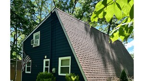 Une maison bleu foncé, dotée d’un toit à forte pente, entourée de pelouse verdoyante et d’arbres.