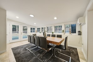 A modern dining area with a large table, chairs, and a view through glass doors.