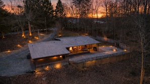 Eine rustikale Holzhütte mit Metallbedachung, umgeben von Bäumen und einem Kiesweg.