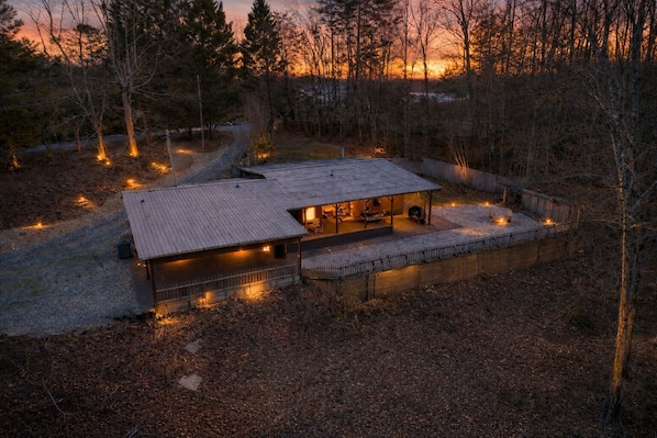 A rustic cabin with a metal roof, surrounded by trees and a gravel path.