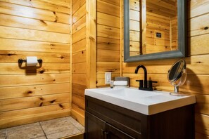 A wooden cabin bathroom with a white sink, a black faucet, a mirror, and a towel dispenser. - 4 Min to Dollywood! Game Room, Indoor Heated Pool, Smoky Mountain Cabin, Hot Tub (Sevierville)