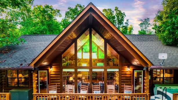 A log cabin with a large glass window, a wooden deck, and a hot tub.