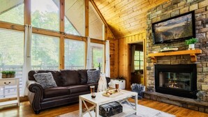 A cozy living room with a stone fireplace, leather sofa, and a television mounted on the wall.