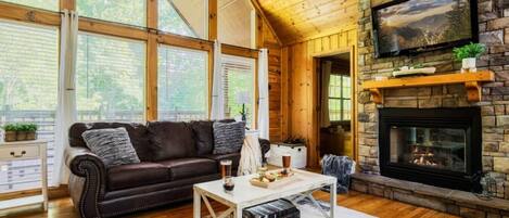 A cozy living room with a stone fireplace, leather sofa, and a television mounted on the wall.